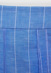 Gros plan sur un tissu bleu avec des rayures blanches verticales fines et des coutures visibles, montrant les détails de la texture et de la couture.