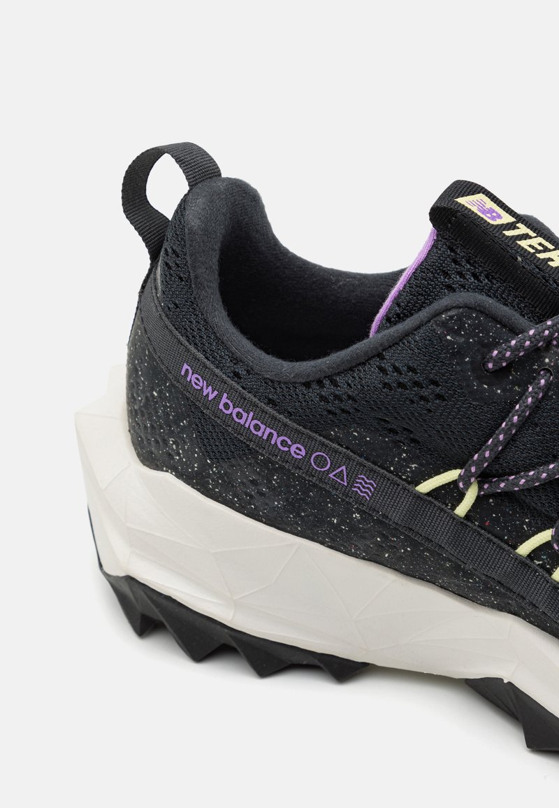 Schwarzer Sportschuh mit strukturiertem Obermaterial, gelben und lila Akzenten, verstärktem Absatz und einer klobigen weißen und schwarzen Sohle. Verfügt über eine Pull-Tab.