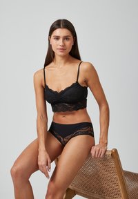 Schwarzer Spitzen-Bralette mit dünnen Trägern und gewelltem Rand. Kombiniert mit passenden schwarzen Spitzenunterhosen, die beide eine weiche Textur haben.