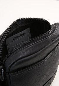 Borsa a tracolla in pelle nera con chiusura a zip, caratterizzata da una texture liscia e un scomparto interno per carte con etichetta del brand.