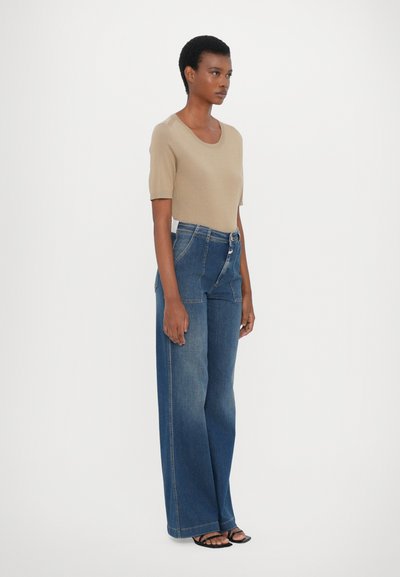 Beige kortermet strikket topp parret med høyhåndte, vide blå denimjeans. Jeansene har et unikt lappet design og en avslappet passform.