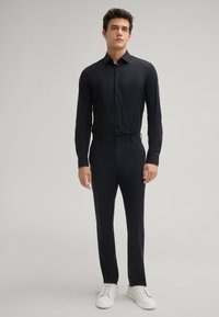 Schwarzes Langarmhemd mit Knopfleiste, kombiniert mit passenden dunklen Hosen und weißen Sneakern, im schlanken Schnitt.