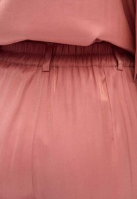 Miękka różowa tkanina o gładkiej fakturze, z elastycznym pasem i subtelnymi fałdami. Projekt zapewnia komfort i swobodę ruchów.