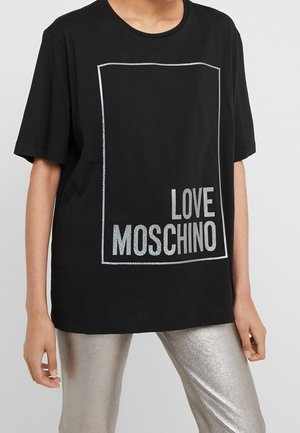 Schwarzes Baumwoll-T-Shirt mit oversized Schnitt, versehen mit einem silbernen Rand und dem Schriftzug "LOVE MOSCHINO" auf der Vorderseite, kombiniert mit schimmernden silbernen Hosen.