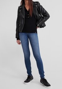 Chaqueta de motorista de cuero negro con herrajes plateados, suéter negro acanalado, jeans ajustados azules y zapatillas negras con suelas blancas.