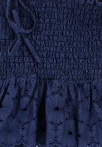 Navyblauwe katoenen stof met geborduurde smocktextuur en bloemenmotieven. Heeft een gerimpelde zoom en een strikdetail bij de hals.