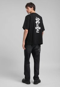 Maglietta nera oversize con design grafico bianco sul retro, abbinata a jeans scuri e scarpe nere chunky. Materiale in cotone morbido.