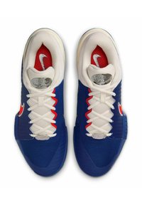 Scarpe da ginnastica blu con tomaia in mesh testurizzato, lacci bianchi, dettagli rossi e un logo metallico sulla linguetta. Suola in gomma con grip.