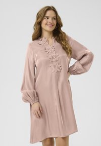 Vestido rosa empolvado hecho de una tela suave, con detalles de encaje floral en el cuello, mangas largas abullonadas y un corte relajado.