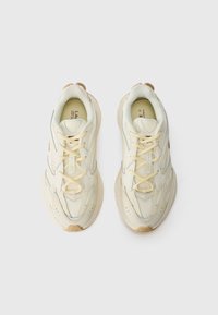 Sneakers met een crèmekleurige synthetische bovenkant, mesh-panelen, beige accenten en ronde veters; dikke zool met gestructureerd detail.