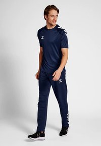 Tamsiai mėlynas sportinis rinkinys, sudarytas iš trumpomis rankovėmis marškinėlių ir kelnių. Pagamintas iš lengvo audinio, su baltu prekės ženklo logotipu ir šoninėmis juostelėmis.