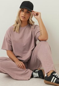 Ljus mauve oversized t-shirt och matchande vida byxor i mjukt tyg. Svart keps och svarta skor med vita ränder fulländar outfiten.