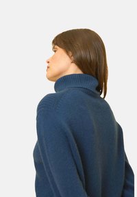 Tmavě modrý rolák s ribbovaným límcem, měkkou texturou a volným střihem, ukazující uvolněný tvar a jemný pletený vzor.