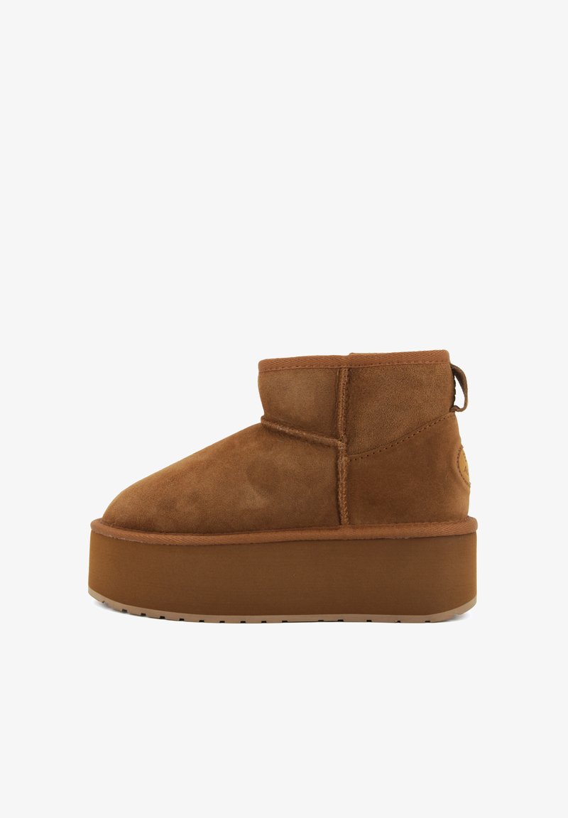 Stivale alla caviglia in suede marrone con punta arrotondata e suola piatta. Caratterizzato da un tacco basso e un anello per un facile utilizzo. Superficie texturizzata con dettagli di cucitura.