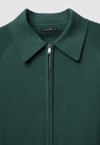 Giacca a zip verde in maglia con colletto, caratterizzata da una zip argentata e texture a coste sulle maniche. Etichetta con scritto "CALLIOPE," taglia S.