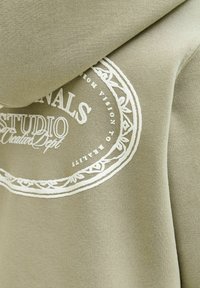 Felpa verde in cotone con un grande emblema bianco stampato che presenta testo decorativo e un design circolare. Texture morbida, vestibilità rilassata.