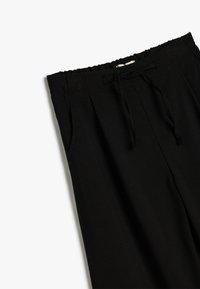 Schwarze, kurze Hose mit einem elastischen Kordelzugbund, seitlichen Taschen und einer glatten Textur. Verfügt über Faltendetails an der Vorderseite.
