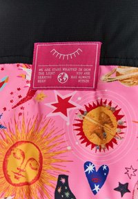 Pestrofarebná ružová textília s nebeskými vzormi, vrátane slnka, hviezd a planét. Ružová etiketa s bielym textom je výrazne zobrazená.