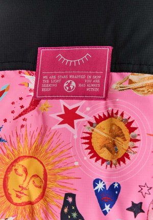 Kolorowy różowy materiał z motywami niebieskimi, w tym słońcami, gwiazdami i planetami. Różowa metka z białym tekstem jest wyraźnie widoczna.