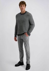 Grijze trui met zigzagpatroon en een geribbelde ronde halslijn, gecombineerd met lichtgrijze broek en zwarte nette schoenen. Eenvoudige, moderne silhouet.