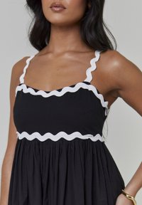 Czarna sukienka z białym, falowanym obszyciem, z cienkimi ramiączkami i marszczoną spódnicą. Gładka bawełniana tkanina, prosty fason i dopasowany górny element.