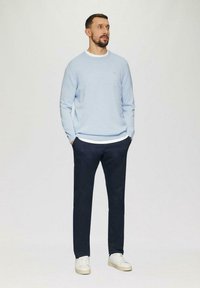 Helles blauer Pullover über einem weißen Rundhalsausschnitt-Shirt, marineblaue Hose und weiße Sneaker; schlichtes Design mit lässiger Passform und weichem Material.