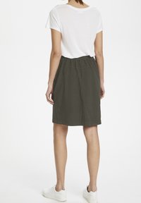 Jupe en lin vert olive foncé avec une taille élastique, longueur genou, associée à une chemise blanche à manches courtes et des baskets blanches.