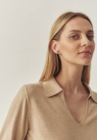 Beige gestrickter Pullover mit V-Ausschnitt und einer weichen, strukturierten Oberfläche. Verfügt über ein geknöpftes Design und sichtbare Nähte.