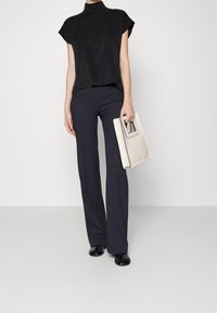 Haut noir à manches courtes avec un col haut, associé à un pantalon large bleu marine. Tient une pochette gris clair avec une anse rectangulaire. Chaussures noires.