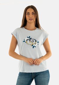 T-shirt azzurro chiaro a maniche corte con orli arrotolati. Presenta un design floreale e il testo "V.7" in colori a contrasto. Tessuto di cotone morbido.