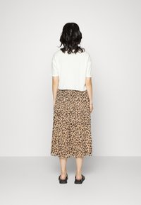 Camiseta blanca cortada combinada con una larga falda plisada de leopardo. Chanclas negras completan el atuendo.