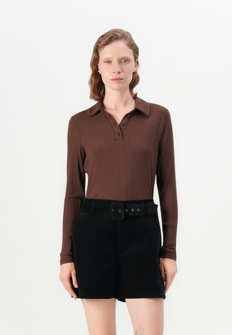 Polo shirt marron à manches longues côtelé avec col, associé à un short noir taille haute avec une ceinture et une boucle.