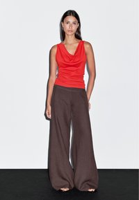 Haut sans manches rouge à col bénitier associé à un pantalon large marron. Tissu doux, coupe décontractée et texture lisse, avec des sandales plates. Design simple.
