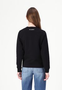 Čierna mikina s dlhými rukávmi, rebrovanými manžetami a okrúhlym výstrihom. Obsahuje biele logo "KARL LAGERFELD" na chrbte.