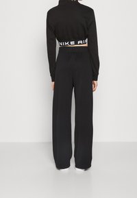 Svart idrottsklädsel som består av en kort jacka med hög krage och vida byxor. Designen inkluderar ett "NIKE AIR" band i vitt på midjebandet.