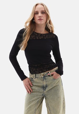 Top nero a maniche lunghe con pannello di pizzo al collo, abbinato a jeans azzurri a vita alta con una textura scolorita e una vestibilità oversize.