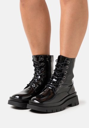 Black patent leather ankle boots with a chunky black platform, silver eyelets, and lace-up design. Smooth texture with a glossy finish.