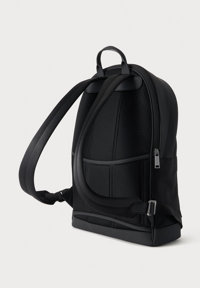 Sac à dos noir avec panneau arrière rembourré, bretelles réglables, poignée supérieure et poche latérale zippée visible de dos sur un fond uni.
