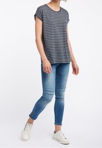 Grå och vit randig kortärmad t-shirt kombinerad med ljusblå skinny jeans och vita sneakers. T-shirten har en rund halsringning och en avslappnad passform.