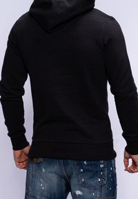 Felpa nera con cappuccio, maniche lunghe, orlo a coste e una superficie liscia. Indossata con jeans in denim strappati.