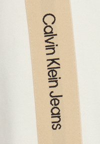 Etichetta Calvin Klein Jeans in testo nero, su uno sfondo di tessuto beige chiaro. L'etichetta presenta un design semplice e minimalista.