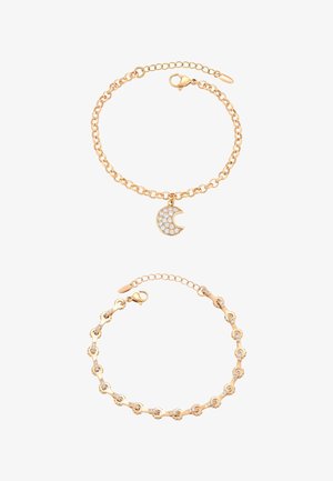 Dwie złote bransoletki łańcuchowe, jedna z zawieszką w kształcie półksiężyca ozdobioną białymi kamieniami, druga z małymi połączonymi elementami dekoracyjnymi.