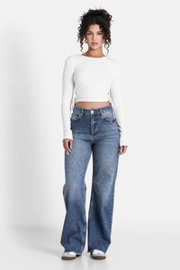 Top blanco de manga larga con canalé y cordones laterales, combinado con jeans de pierna ancha de tiro alto en azul claro y zapatillas blancas.
