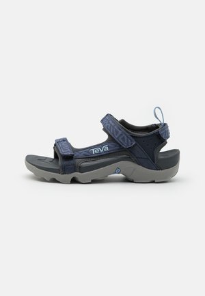 Marineblauwe sandal met verstelbare banden, grijze rubberen zool, gestructureerde bovenkant en achterste trekband. Kenmerkt het Teva-logo aan de zijkant.