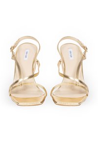 Złote metaliczne sandały na wysokim obcasie z krzyżującymi się paskami, odkryty palec i prostokątny obcas. Posiadają zapięcie na klamrę przy pasku na kostce.