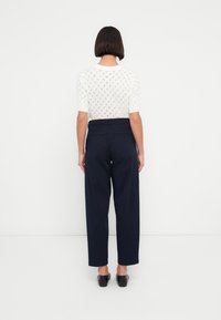 Λευκό πλεκτό πουλόβερ με κοντά μανίκια και σχέδιο με ρόμβους, συνδυασμένο με ψηλόμεσο μπλε σκούρο παντελόνι, που διαθέτει δύο πίσω τσέπες και ίσια εφαρμογή.