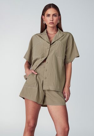 Khaki dvoudílný oblek obsahující košili na knoflíky s krátkým rukávem a velkými kapsami, spolu s odpovídajícími šortkami, oboje s kontrastním prošíváním.