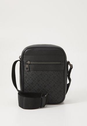 Sac bandoulière noir avec motif de logo texturé, accents en cuir et sangle en tissu réglable. Comprend une poche frontale zippée.
