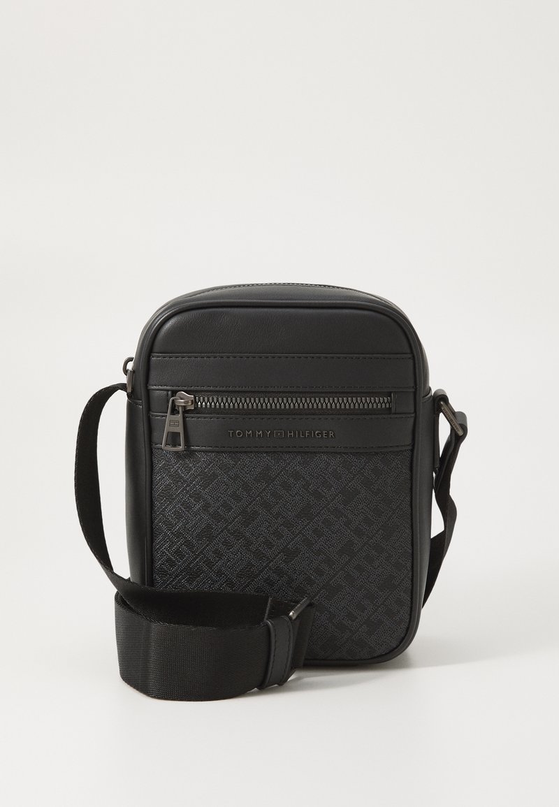 Bolso bandolera negro con un patrón de logo texturizado, detalles en cuero y correa de tela ajustable. Incluye un bolsillo frontal con cremallera.