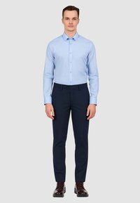 Camicia azzurro chiaro a maniche lunghe con colletto a scatto, abbinata a pantaloni navy e scarpe eleganti marroni. Tessuto morbido, vestibilità su misura.